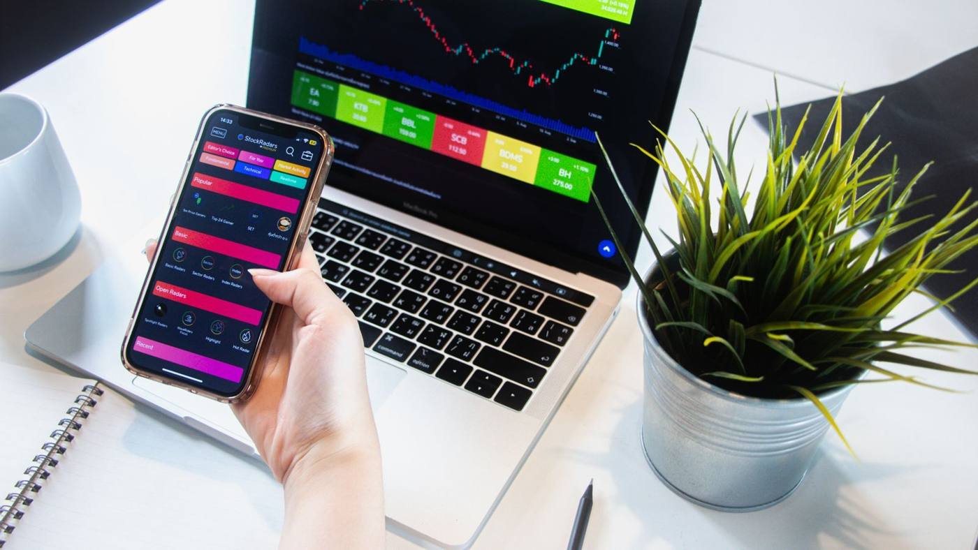 A hand holding a phone and testing an app, at a desk.